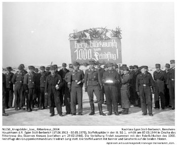 Hauptmann d.R. Egon Stoll-Berberich (17.06.1913 - 02.05.1973), Staffelkapitän in der III. SG 1,  erhält am 07.03.1944 in Orscha das Ritterkreuz des Eisernen Kreuzes (verliehen am 29.02.1944). Die Verleihung findet zusammen mit den Feierlichkeiten des 1000. Feindflugs des Gruppenkommandeurs Friedrich Lang statt. Die Staffel mit ihrem neuen Ritterkreuzträger. NLESB_Kriegsbilder_lose_Ritterkreuz_0004