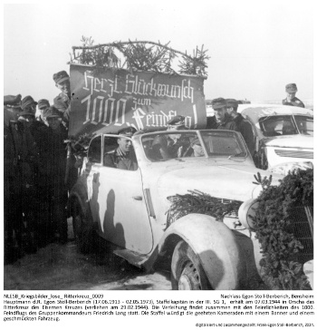 Hauptmann d.R. Egon Stoll-Berberich (17.06.1913 - 02.05.1973), Staffelkapitän in der III. SG 1,  erhält am 07.03.1944 in Orscha das Ritterkreuz des Eisernen Kreuzes (verliehen am 29.02.1944). Die Verleihung findet zusammen mit den Feierlichkeiten des 1000. Feindflugs des Gruppenkommandeurs Friedrich Lang statt. Die Staffel würdigt die geehrten Kameraden mit einem Banner und einem geschmückten Fahrzeug. NLESB_Kriegsbilder_lose_Ritterkreuz_0009