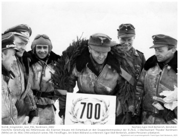 Feierliche Verleihung des Ritterkreuzes des Eisernen Kreuzes mit Eichenlaub an den Gruppenkommandeur der III./St.G. 1 Oberleutnant Theodor Nordmann (Mitte) am 16. März 1943 anlässlich seines 700. Feindfluges. Am linken Bildrand zu erkennen: Egon Stoll-Berberich, andere Personen unbekannt. NLESB_Kriegsbilder_lose_P06_Nordmann_0002.