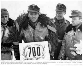Feierliche Verleihung des Ritterkreuzes des Eisernen Kreuzes mit Eichenlaub an den Gruppenkommandeur der III./St.G. 1 Oberleutnant Theodor Nordmann (Mitte) am 16. März 1943 anlässlich seines 700. Feindfluges. Am linken Bildrand zu erkennen: Egon Stoll-Berberich, andere Personen unbekannt. NLESB_Kriegsbilder_lose_P06_Nordmann_0003.